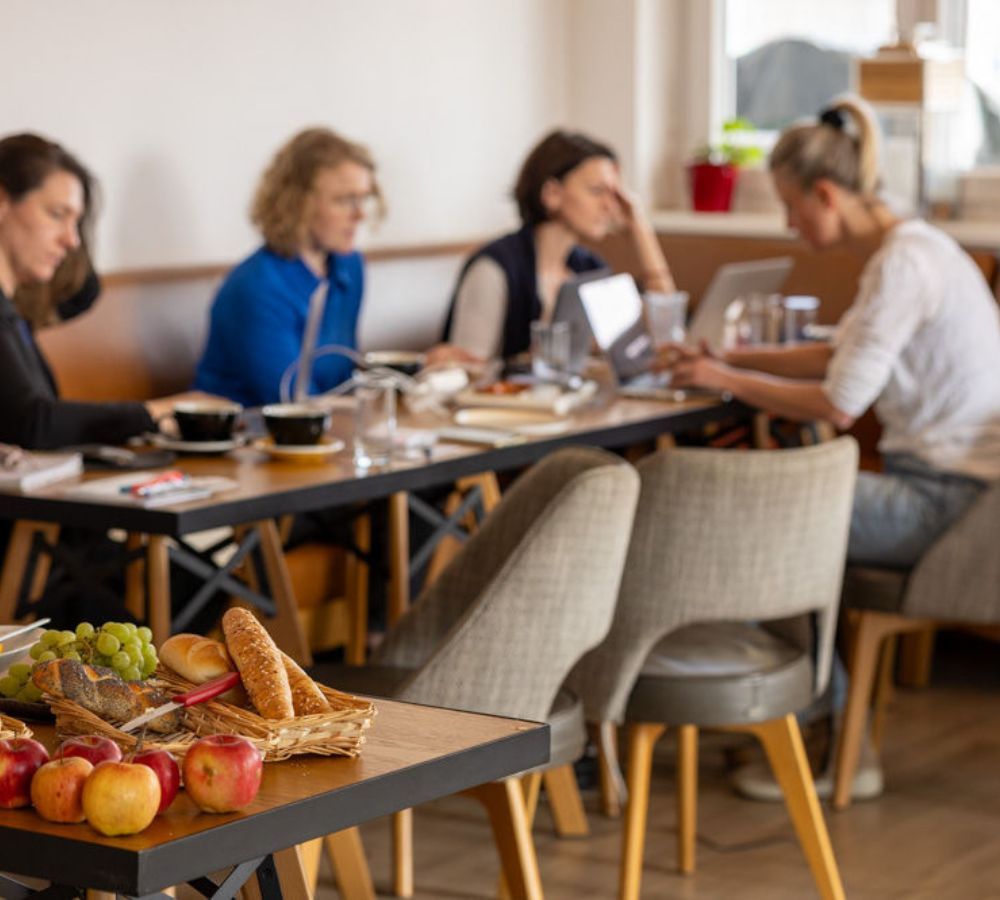 Foto von Birgit Lauss. Man sieht ein Netztwerkevent in einem Cafe. Einige Damen sitzen um einen Tisch und arbeiten. Daneben ein Buffet