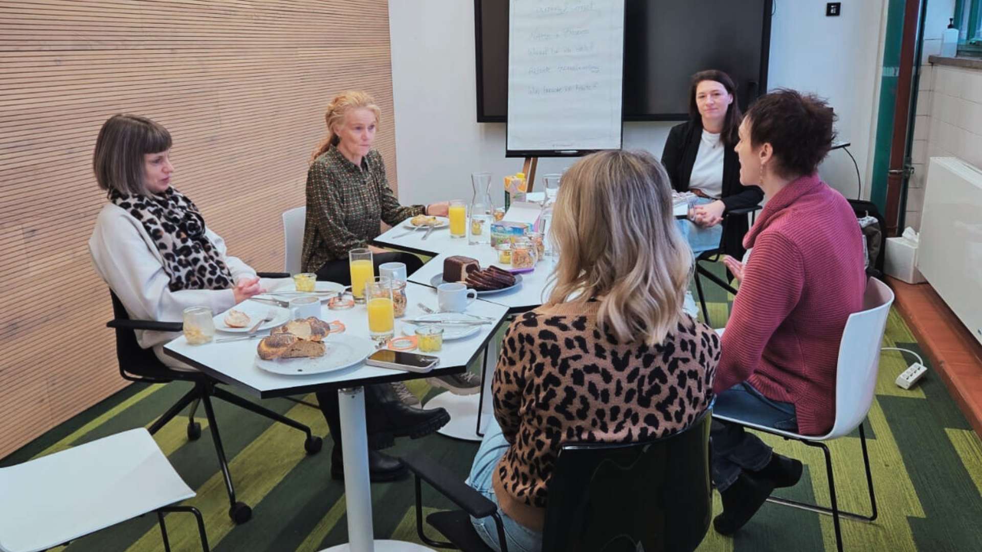 5 Frauen sitzen um eine Tischgruppe und frühstücken